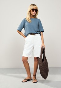 Top in lino azzurro chiaro a maniche corte, pantaloncini bianchi su misura, sandali neri con cinturini e borsa a tracolla intrecciata marrone. Design semplice e moderno.