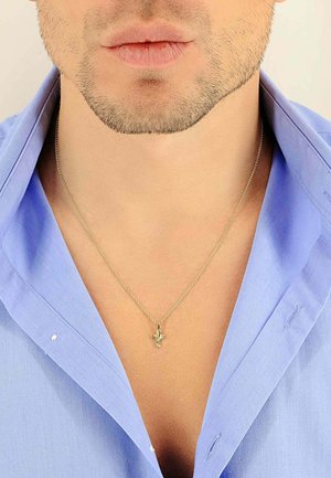 Collier en chaîne argentée avec un petit pendentif en forme de croix porté sur une chemise à col bleu clair, mettant en valeur une texture de tissu lisse et un design classique.