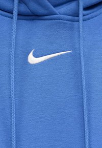 Ύφασμα μπλε φούτερ με λευκό κεντητό λογότυπο Nike swoosh στο κέντρο ανάμεσα σε δύο κορδόνια.