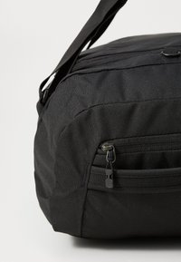 Borsa in tessuto nero con tasca con zip, forma curvata, superficie texturizzata e tracolla regolabile. Presenta cuciture discrete e dettagli metallici.