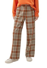 Geruite broek in bruin, oranje en crème kleuren; hoge taille met een rechte pijp en zijzakken, gedragen met witte sneakers.