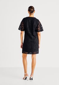 Μαύρο μίνι φόρεμα από δαντέλα με κοντά μανίκια και υφή με κομμένο τελείωμα. Φοριέται με ασημένιες ψηλοτάκουνες σάντες.