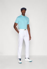 Lyseblå polo skjorte, hvite bukser, og hvite golfsko med blå detaljer. Båret med en marineblå caps. Enkel design, glatt tekstur.