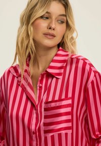 Jedwabna koszula z pionowymi czerwonymi i różowymi paskami, z ostro zakończonym kołnierzykiem, kieszenią na piersi z przodu oraz guzikami z przodu.