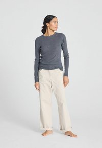 Cămașă gri cu mâneci lungi și guler rotund, asortată cu pantaloni bej cu croi larg. Ținuta are o siluetă relaxată și o textură moale.