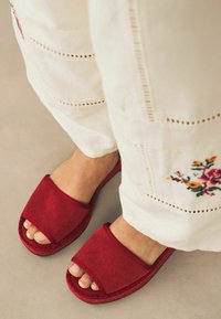 Rode stoffen slip-on sandalen met een brede band, textuurafwerking en platte zool, gecombineerd met witte geborduurde broek.