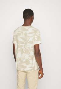 Béžové maskáčové tričko s krátkým rukávem, kulatým výstřihem a uvolněným střihem. Měkká bavlněná tkanina s jemnými tónovými variacemi v vzoru.