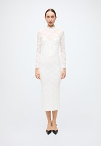 White lace long-sleeve dress with sweetheart neckline, fitted silhouette, and mid-calf length. Black pointed-toe heels complete the look.