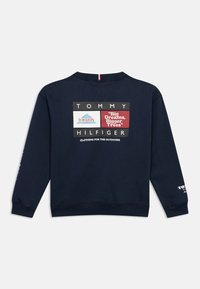Granatowa bluza z logo Tommy Hilfiger, grafiką gór oraz napisami „Big Dreams, Bigger Trees” i „Clothing for the Outdoors” na plecach.