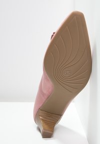 Scarpa con tacco alto in suede rosa, dotata di un tacco curvo e texturizzato e di una suola in gomma liscia, caratterizzata da un design a motivo per migliorare la trazione.