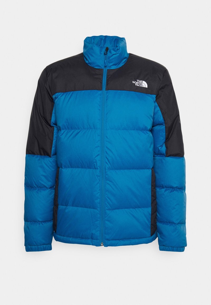 Niebieska kurtka puchowa z czarnym panelem na ramieniu, wysokim kołnierzem, zapięciem na zamek i pikowaną teksturą. Posiada logo na lewej piersi.