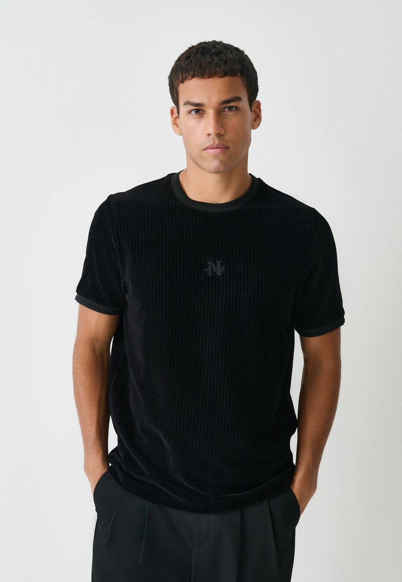 Schwarzes Cord-T-Shirt mit kurzen Ärmeln, gerippter Textur, rundem Halsausschnitt und subtil eingesticktem Logo auf der Brust. Passender dunkler Besatz.