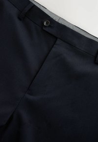 Pantalon de costume bleu marine foncé avec une coupe plate, fermeture à un bouton et une texture subtile. Il présente une ceinture intérieure à motif.