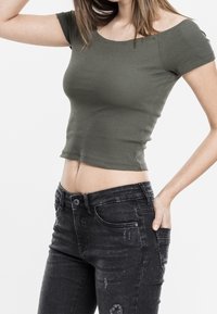 Olivově zelený žebrovaný crop top s krátkými rukávy, kombinovaný s potrhanými černými jeansy s vysokým pasem, zdůrazňujícími přiléhavý střih.