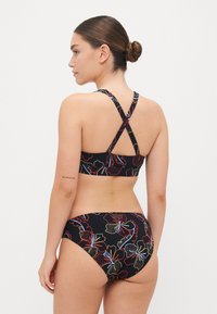 Bikini noir avec des motifs floraux en rouge, jaune et bleu. Design croisé au dos pour le haut, avec un bas taille basse affichant une marque.
