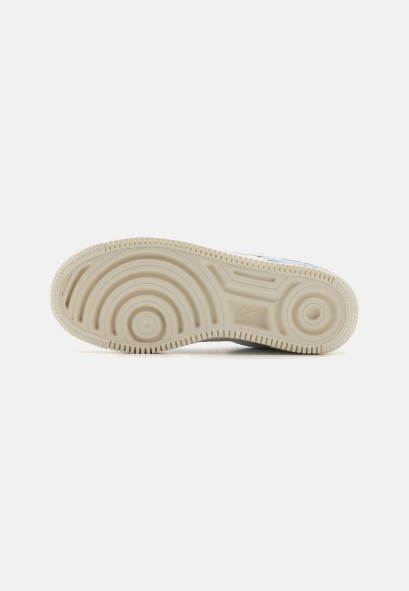 Semelle de chaussure présentant un design texturé avec des motifs circulaires, principalement beige avec des accents clairs, fabriquée en matériau en caoutchouc durable.
