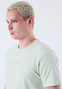 T-shirt verde chiaro a maniche corte con scollatura rotonda e tessuto testurizzato. Presenta un sottile logo "PXP" sul petto.