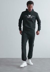 Must have mustri kappa ja sobivad püksid, mis sisaldavad esist taskut ja logo detaile, koos valgete tossudega. Sile kangas ja sportlik istuvus.