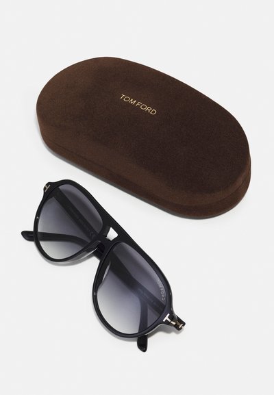Ochelari de soare negri cu lentile degradate, însoțiți de un toc moale maro, cu brandul "TOM FORD" în aur. Textură netedă, design elegant.