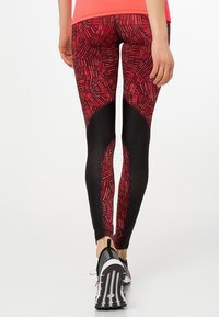Czarno-czerwone legginsy sportowe z wzorem, o dopasowanym kroju, z teksturowanymi panelami i geometrycznym wzorem. Noszone z czarno-białymi sneakersami.