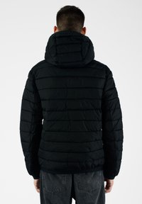 Giacca a vento nera con cappuccio, caratterizzata da linee trapuntate orizzontali e polsini elasticizzati. Texture liscia e design leggero.