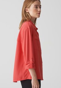 Camicia a maniche lunghe color corallo con colletto, tasca frontale singola, maniche arrotolate e vestibilità morbida. Tessuto morbido e design con orlo dritto.