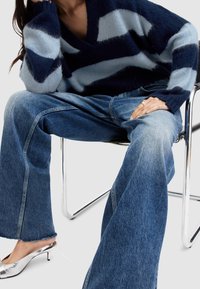 Gruby, paskowany sweter z granatowego i jasnoniebieskiego moheru. Szerokie dżinsy o szerokich nogawkach z postrzępionym wykończeniem. Srebrne szpilki w szpic.