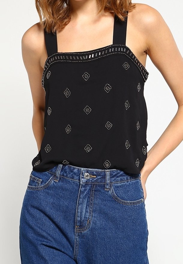 Top nero senza maniche con scollatura quadrata, decorato con motivi a diamante argentati e un rifinitura testurizzata, abbinato a jeans a vita alta blu.