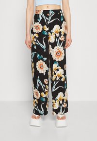 Pantalons à jambes larges en tissu noir avec de grands motifs floraux orange, blancs et bleus canard. Texture lisse et taille mi-haute.