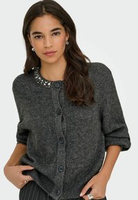 Tumehall kardigan kolmeveerandiliste varrukatega, ümmargune kaelus, mis on kaunistatud sädelevate kivikestega, kuus nööbisuletust ja soonikkoes äär. Pehme tekstuur.