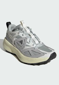 Light gray athletic shoes with mesh and synthetic overlay, textured toe cap, prominent lacing system, and black heel tab. Features cushioning midsole.