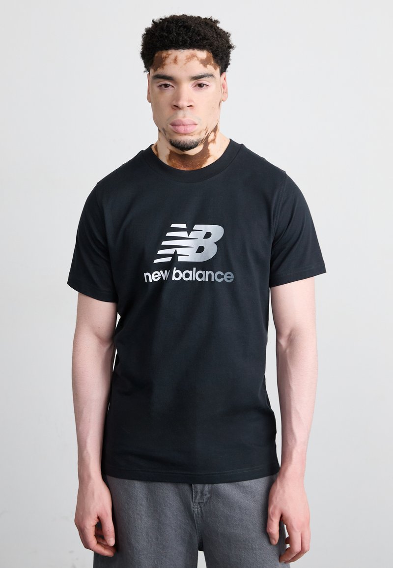 T-shirt in cotone nero con logo "New Balance" argentato sul davanti. Il design include maniche corte e collo rotondo.