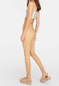 Tan skinny jeans med hög midja, med en slät textur och minimal sömnad. Matchas med ljusfärgade platåsandaler.