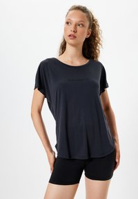 Sort kortærmet t-shirt med en scoop halsudskæring og teksten "Jeg er på et nyt niveau" på fronten. Sammen med sorte tætsiddende shorts.