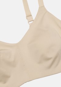 Beige bh med mjukt, texturerat tyg, justerbara axelremmar och sömlös design. Har en subtil glans och minimal sömnadsdetaljer.