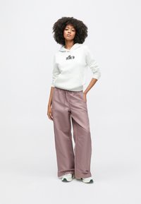 Ανοιχτό γκρι φούτερ με κουκούλα και μπροστινή τσέπη, με μαύρο λογότυπο, σε συνδυασμό με φαρδιά μωβ παντελόνια με ελαστική μέση και λευκά αθλητικά παπούτσια.