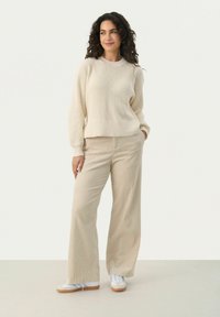 Beige ribbeltrui met een ronde hals en lange mouwen, gecombineerd met brede beige corduroy broek en witte sneakers. Casual outfit.