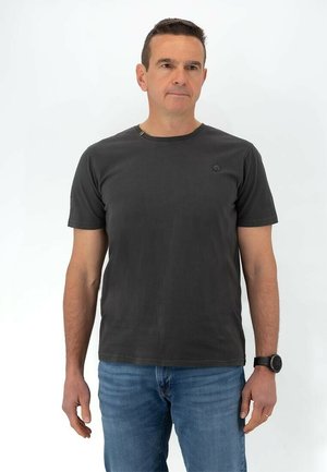 T-shirt grigio a maniche corte con colletto rotondo e un piccolo logo sul petto, abbinato a jeans blu. Tessuto liscio, vestibilità casual.