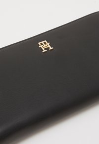 Black leather wallet featuring a gold-tone logo accent. Smooth texture with clean lines and compact design, ideal for organization.
