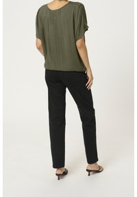 Top verde oliva a maniche corte con vestibilità comoda e tessuto testurizzato, abbinato a pantaloni neri slim fit e sandali con tacco neri.