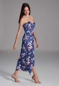 Vestido floral sin tirantes en azul marino con flores blancas y rojas. De longitud media, con tela fluida y un ligero brillo, acompañado de tacones nude con tiras.