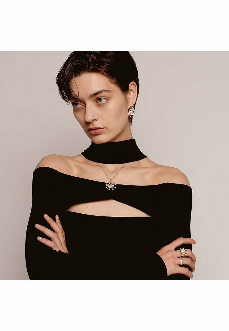 Schwarzes Off-Shoulder-Oberteil mit einem Ausschnitt-Design, kombiniert mit einer blumigen Anhänger-Halskette, passenden Ohrringen und Ringen mit ähnlichen Mustern.