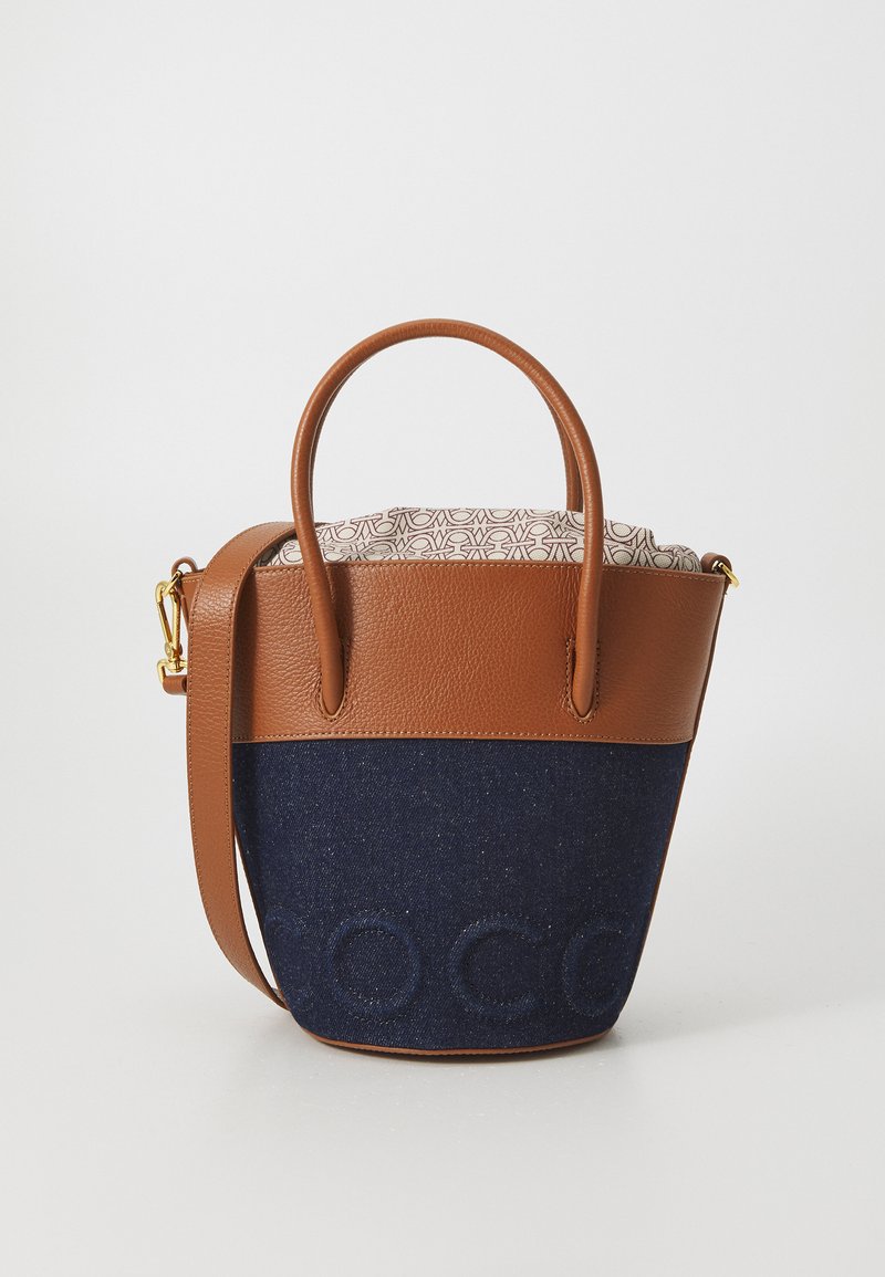Brown leather and navy denim bucket bag with short handles, adjustable strap, and tan interior featuring a patterned lining.