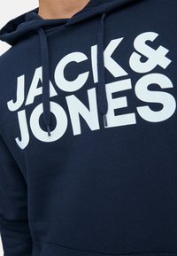 Navy blue hoodie made of cotton, featuring a large white logo text "JACK & JONES" on the front. Includes a hood and drawstrings.