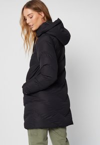 Chaqueta acolchada negra con capucha, presenta costuras diagonales y un ajuste ligeramente holgado. Material ligero con textura suave.