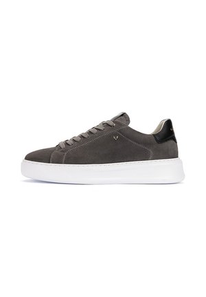 Zapatilla gris de ante de caña baja con la lengüeta negra en el talón, cordones grises y suela blanca gruesa, mostrada sobre un fondo blanco.