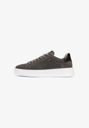 Zapatilla gris de ante de caña baja con la lengüeta negra en el talón, cordones grises y suela blanca gruesa, mostrada sobre un fondo blanco.