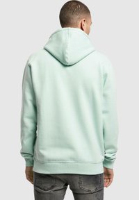 Mintgrüner Hoodie mit großer Rückentasche, verstellbarem Kordelzug an der Kapuze, gerippten Ärmelbündchen und Saum, aus weichem Baumwollmischgewebe.