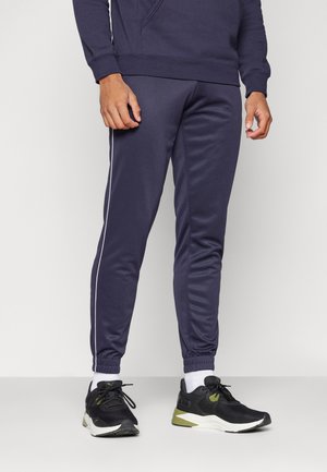 Navyblaue Jogginghosen mit weißen Seitenstreifen, elastischen Bündchen und einer glatten Textur, kombiniert mit schwarzen Laufschuhen und weißen Socken.