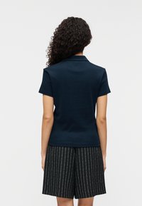 Polo à manches courtes bleu marine avec un col classique, présentant une texture lisse et une silhouette ajustée, associé à un short noir rayé.